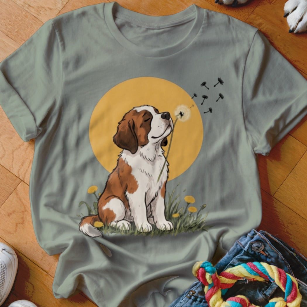 A sage green t-shirt featuring a graphic of a Saint Bernard puppy blowing dandelion seeds.