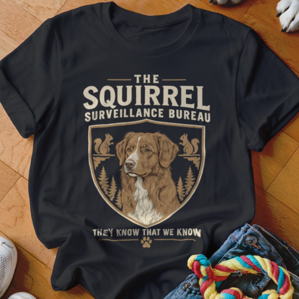 A black t-shirt printed with a dog crest and text reading The Squirrel Surveillance Bureau.