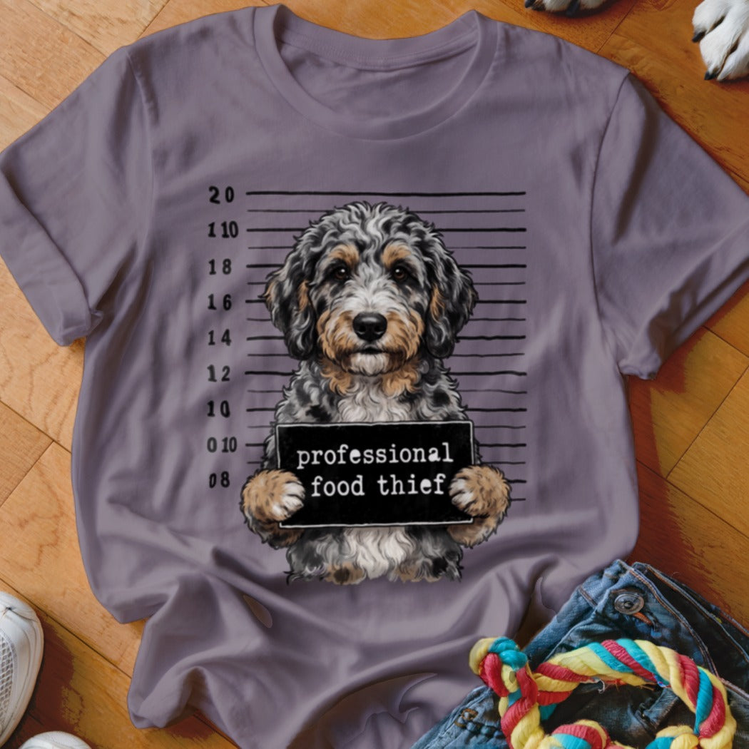 Doodle dog mugshot with "professional food thief" sign on a gray t-shirt.