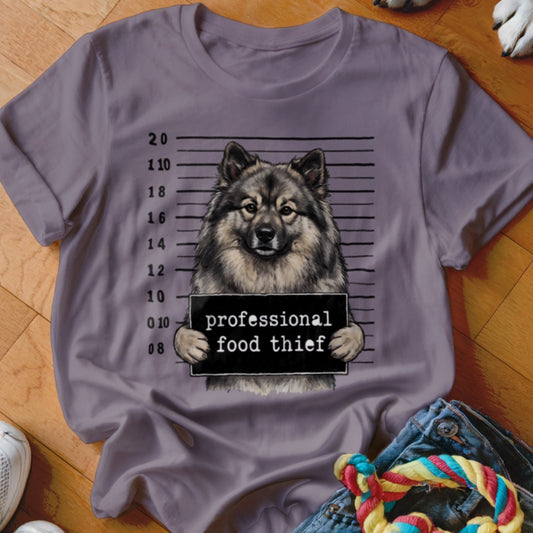 Keeshond dog mugshot sign reads "professional food thief" on t-shirt.