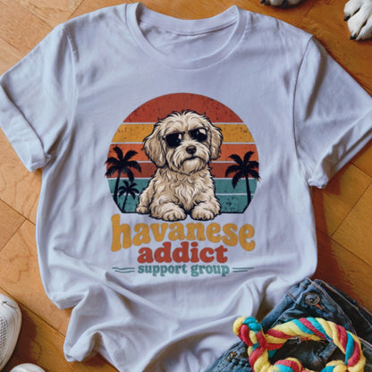 A white t-shirt featuring a graphic of a Havanese dog in sunglasses with sunset and palm tree graphics.