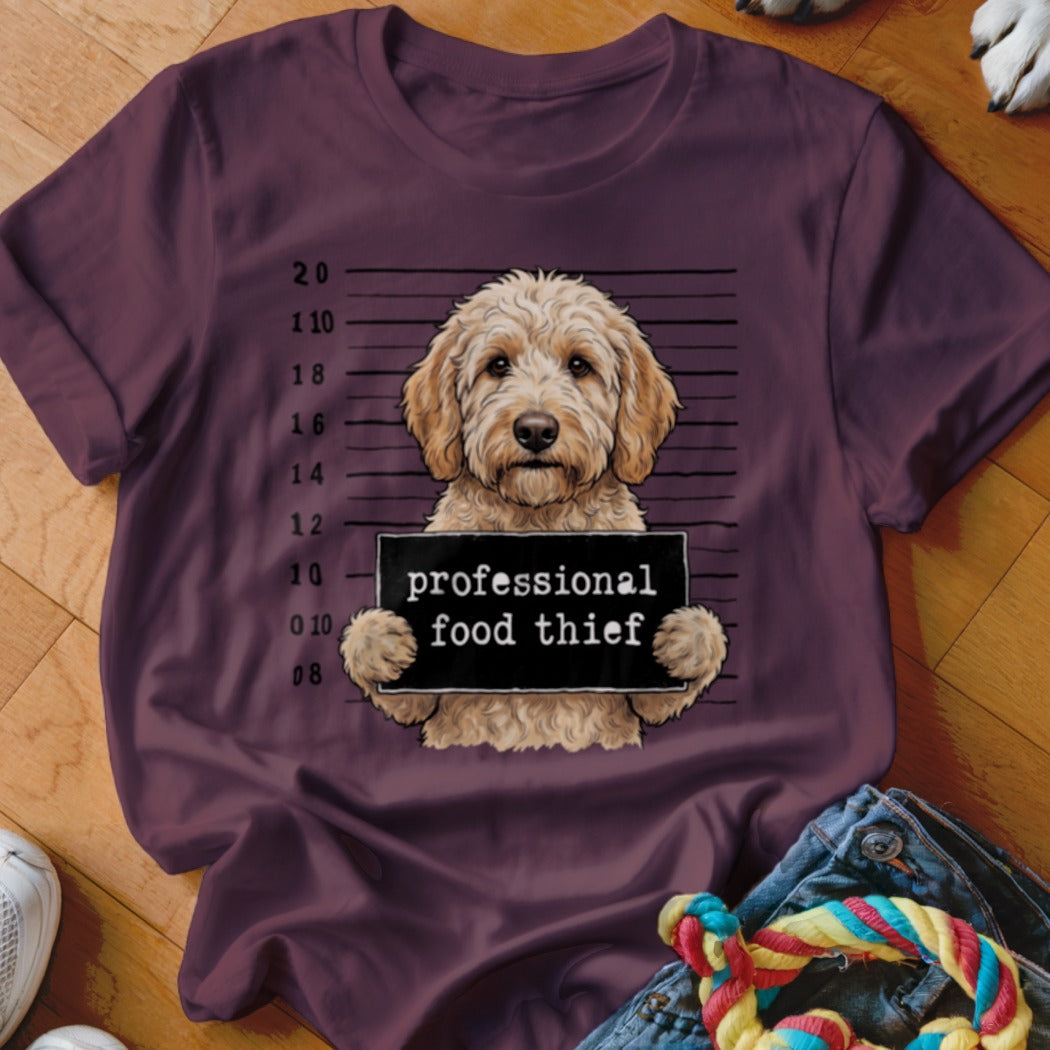 Goldendoodle mugshot graphic with "professional food thief" sign on a maroon t-shirt.