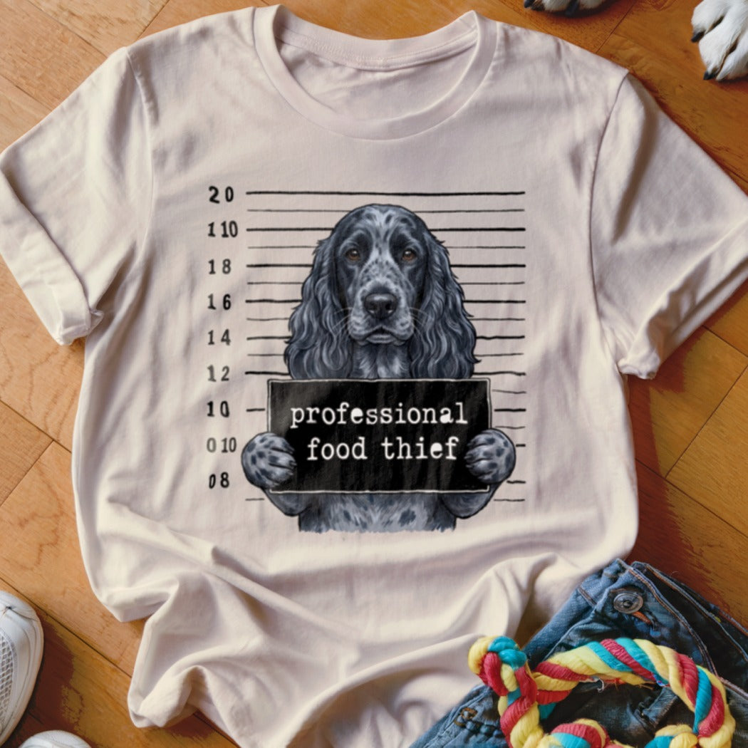 T-shirt graphic of a dog with a mugshot sign that reads "professional food thief".