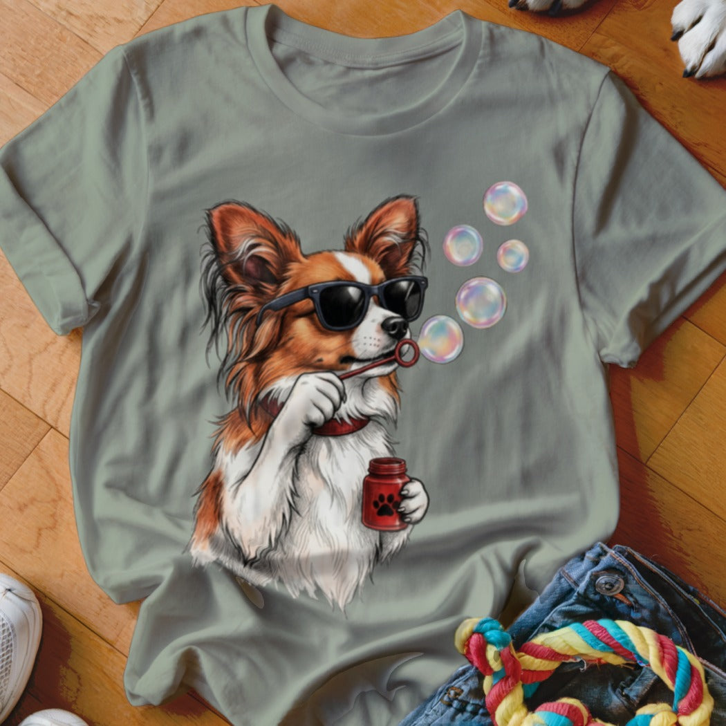 A sage green crewneck t-shirt featuring a graphic of a brown and white dog wearing sunglasses while blowing soap bubbles.