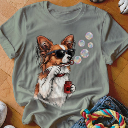 A sage green crewneck t-shirt featuring a graphic of a brown and white dog wearing sunglasses while blowing soap bubbles.