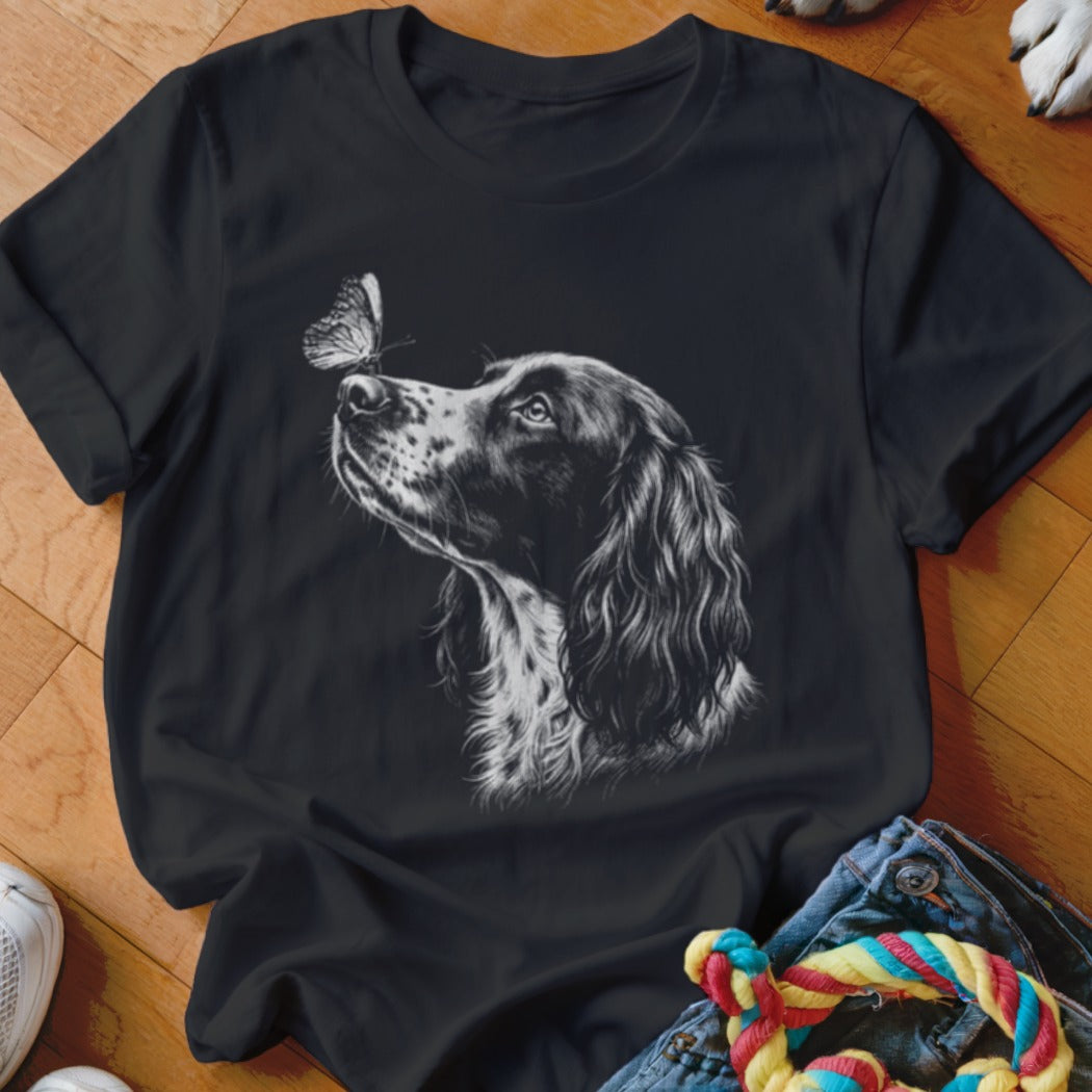 Black crewneck t-shirt featuring a white sketch graphic of a spaniel dog looking at a butterfly on its nose.