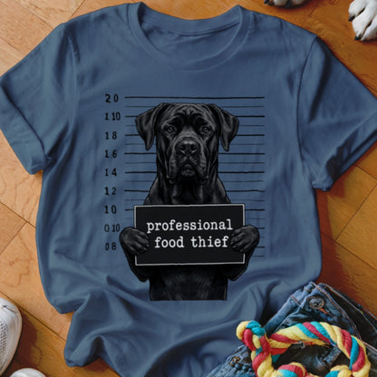 Black dog in mugshot holding "professional food thief" sign on navy t-shirt.