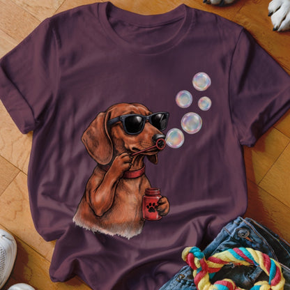 A dark purple crewneck t-shirt featuring a dachshund wearing sunglasses and blowing soap bubbles.