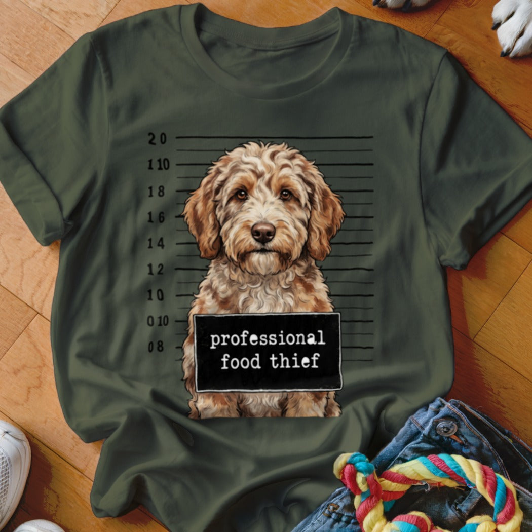 Dog mugshot with "professional food thief" sign on a green t-shirt.