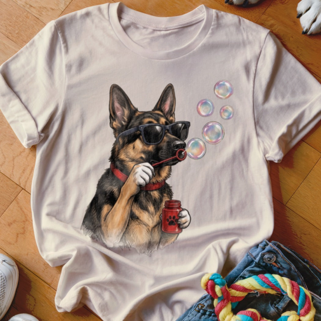 A light pink t-shirt printed with a German Shepherd wearing sunglasses and blowing soap bubbles.