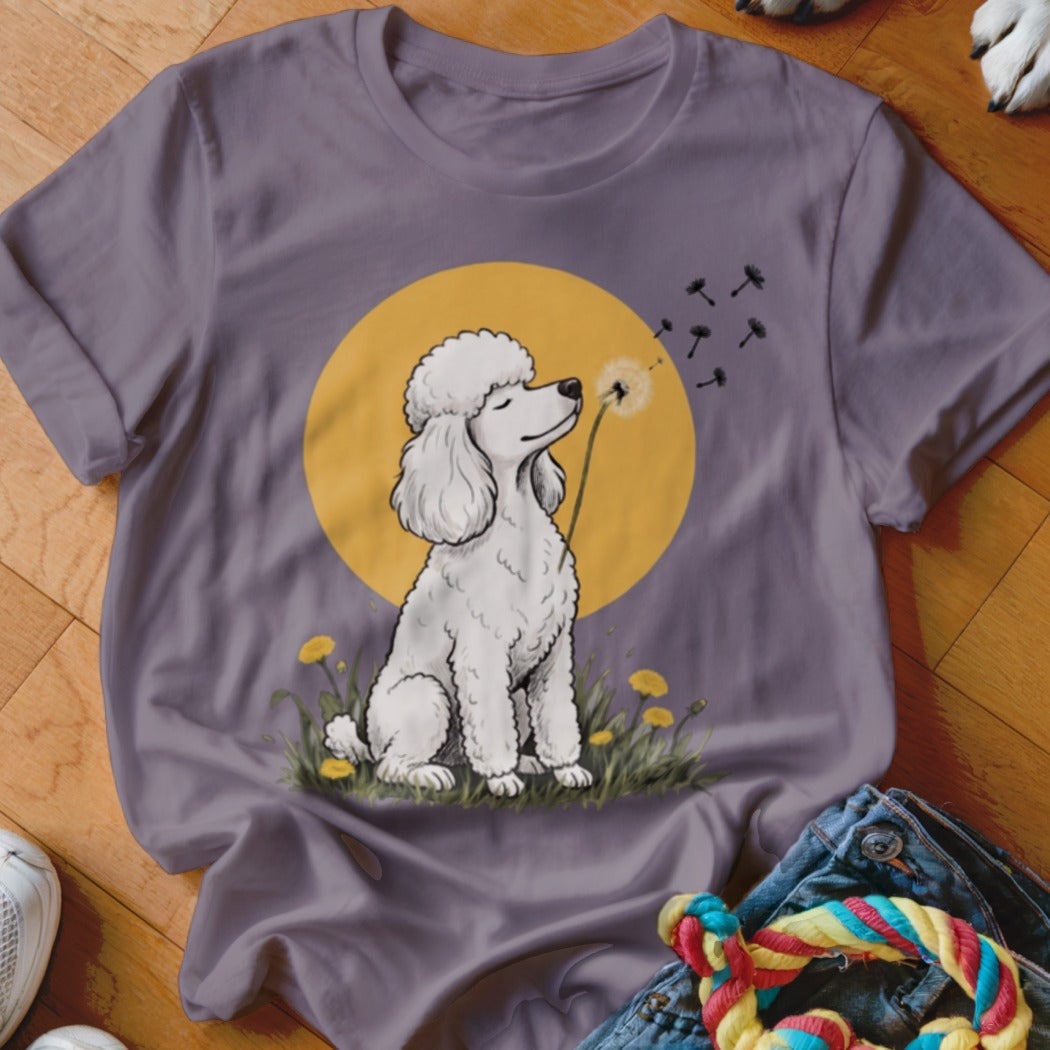 Mauve t-shirt featuring a cartoon illustration of a white poodle sitting in grass and blowing a dandelion.