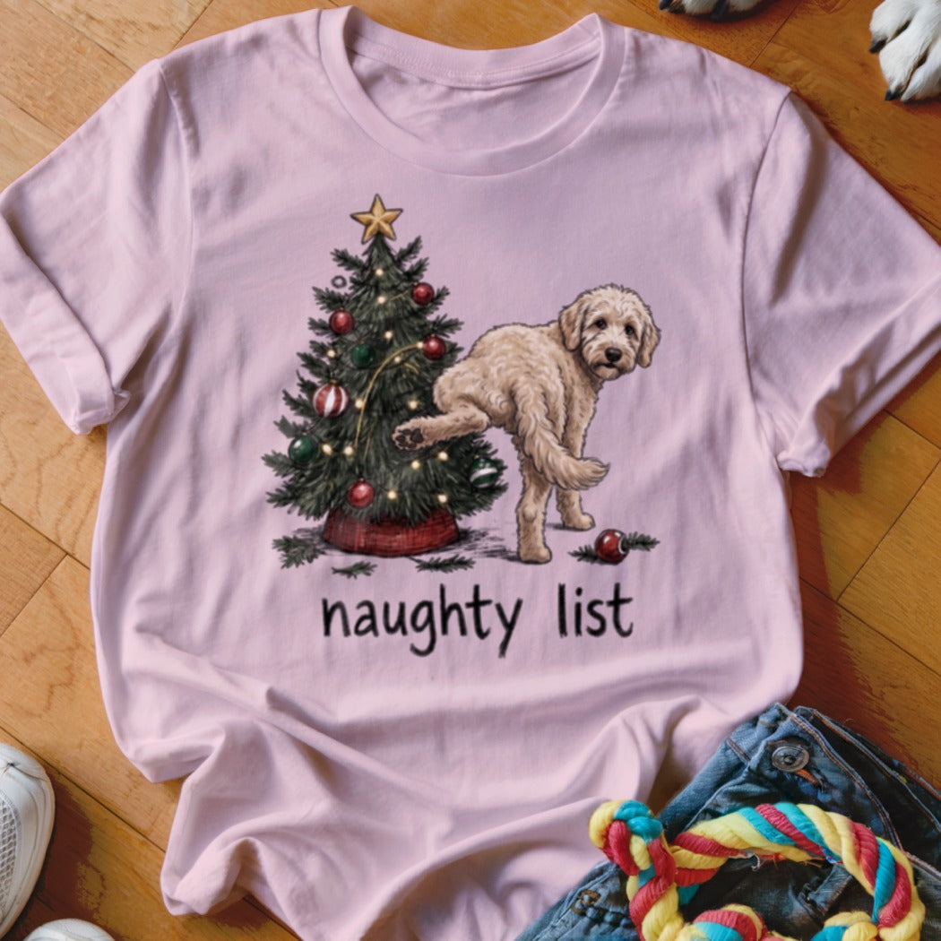 Light pink t-shirt with a cartoon dog lifting its leg on a Christmas tree with "naughty list" text.