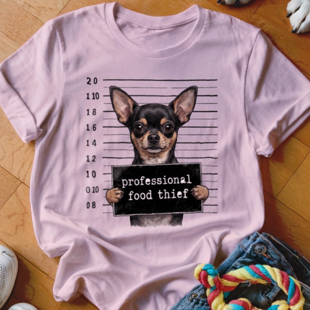 Chihuahua mugshot with "professional food thief" sign on pink t-shirt.