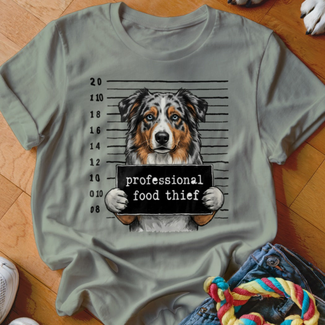 Australian Shepherd in mugshot holding "professional food thief" sign