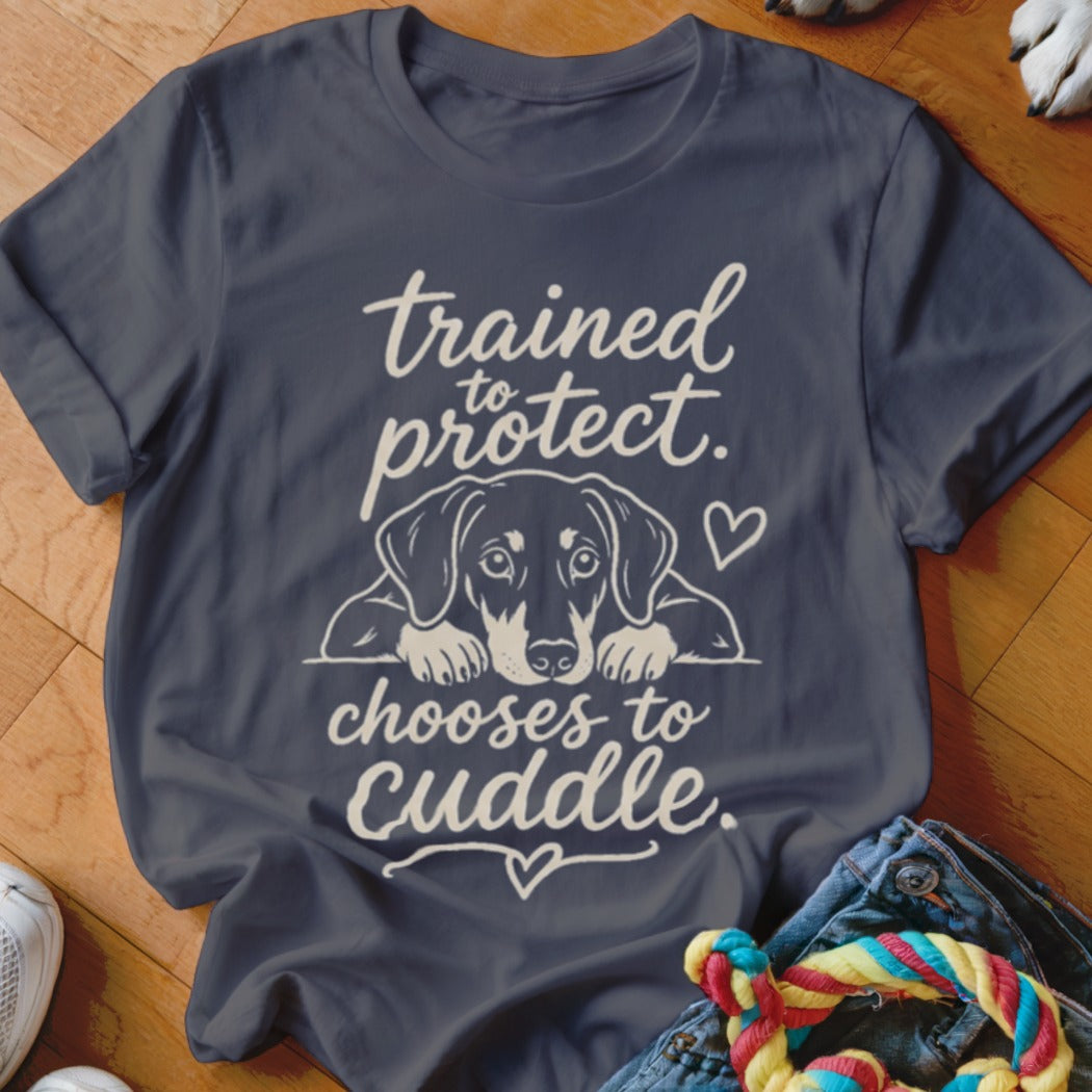 Dark t-shirt with a dachshund graphic and text: "trained to protect. chooses to cuddle."