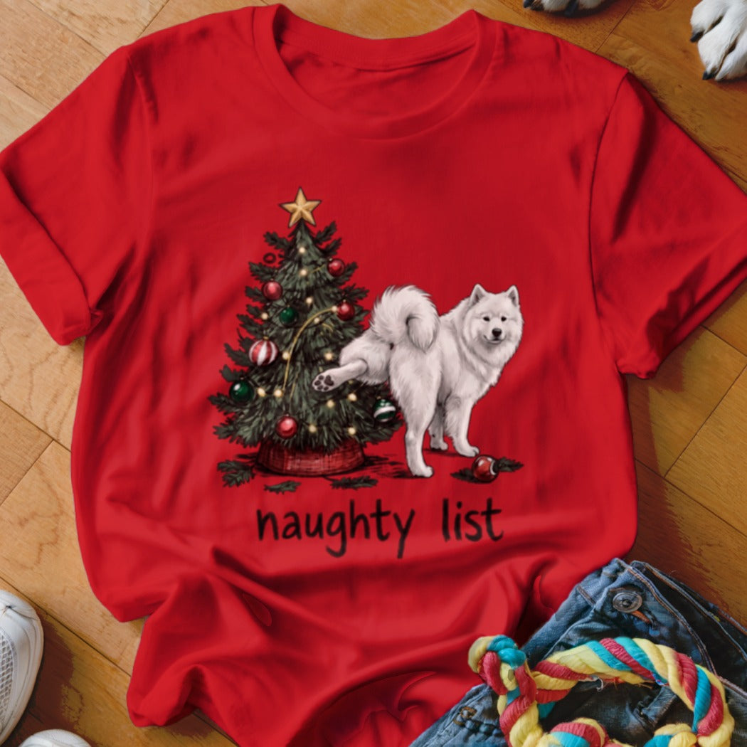 A red t-shirt printed with a white Samoyed dog peeing on a decorated Christmas tree above the text "naughty list".
