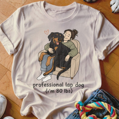 Cream t-shirt with cartoon of a person hugging a Rottweiler dog, text reads "professional lap dog (I'm 80 lbs)".