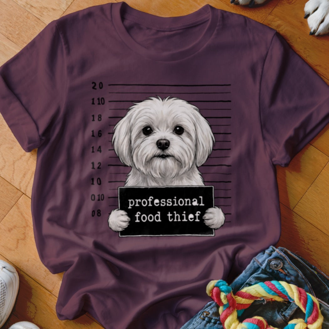 Maltese dog in mugshot holding a sign that reads "professional food thief".