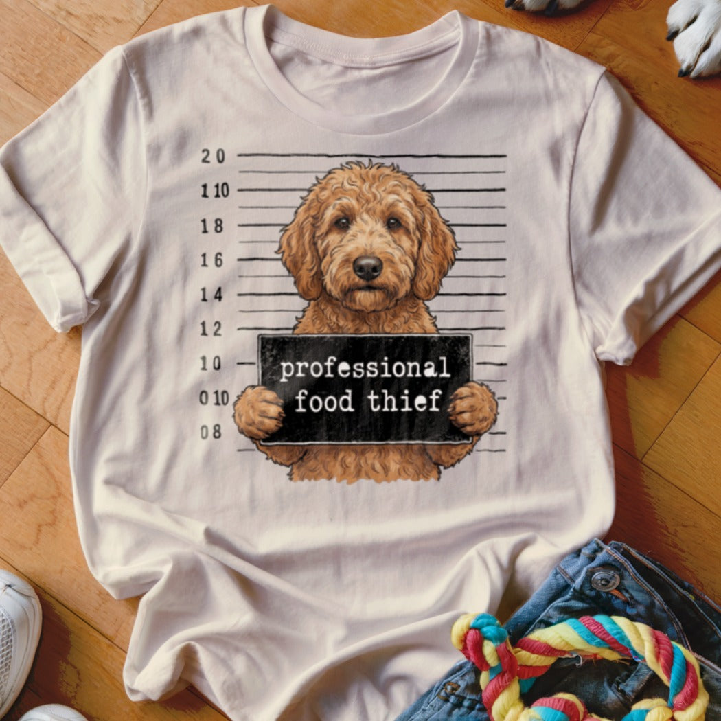 Goldendoodle dog mugshot with "professional food thief" text on a t-shirt.