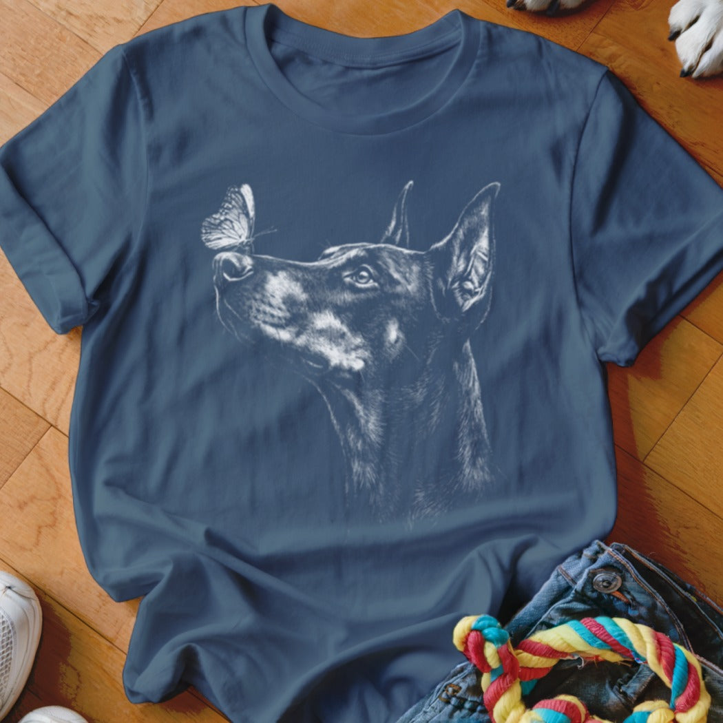 A blue t-shirt featuring a white sketch of a Doberman Pinscher looking up at a butterfly on its nose.