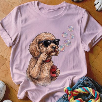 A light pink t-shirt featuring an illustration of a fluffy golden dog wearing sunglasses and blowing bubbles.