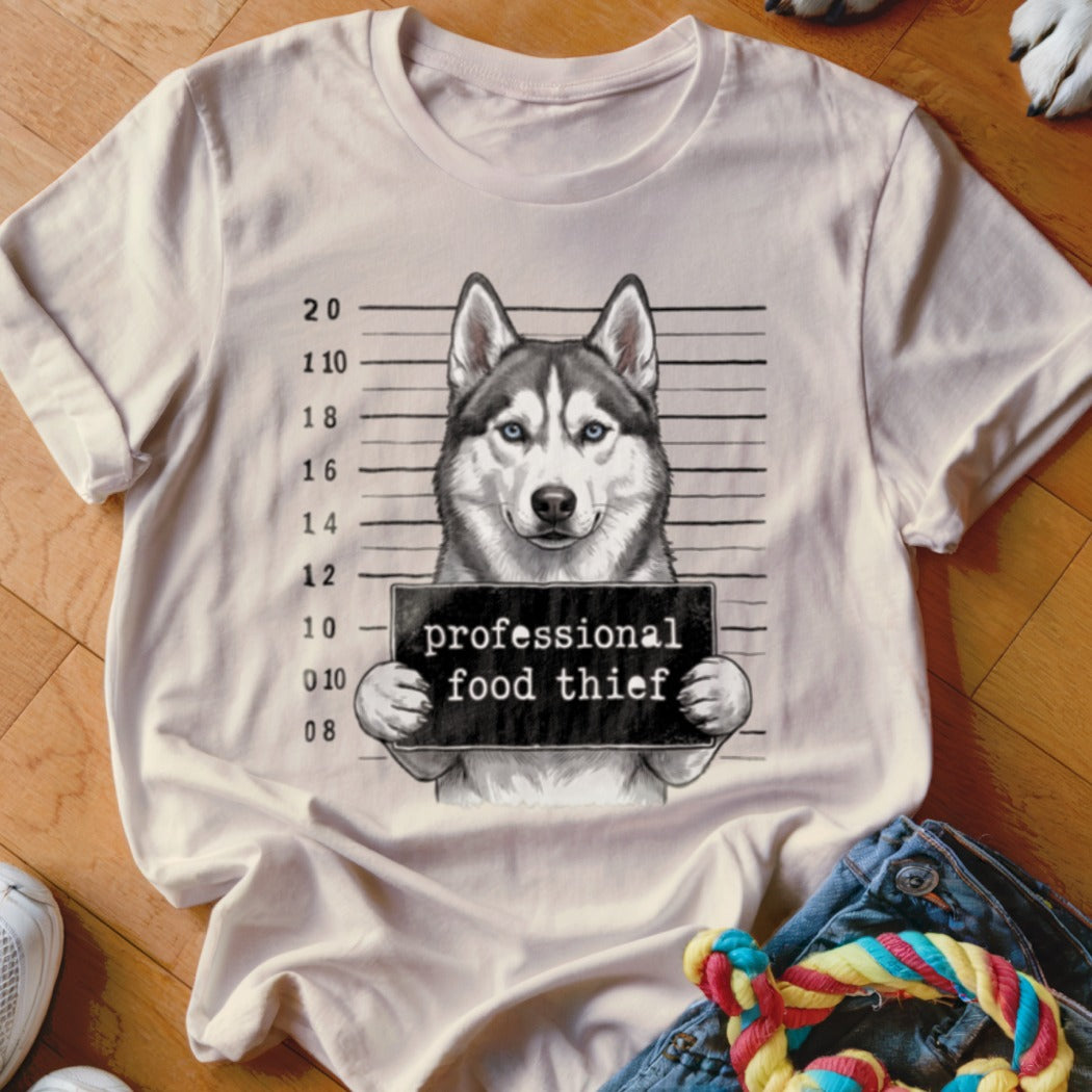 Husky dog in mugshot holding "professional food thief" sign.