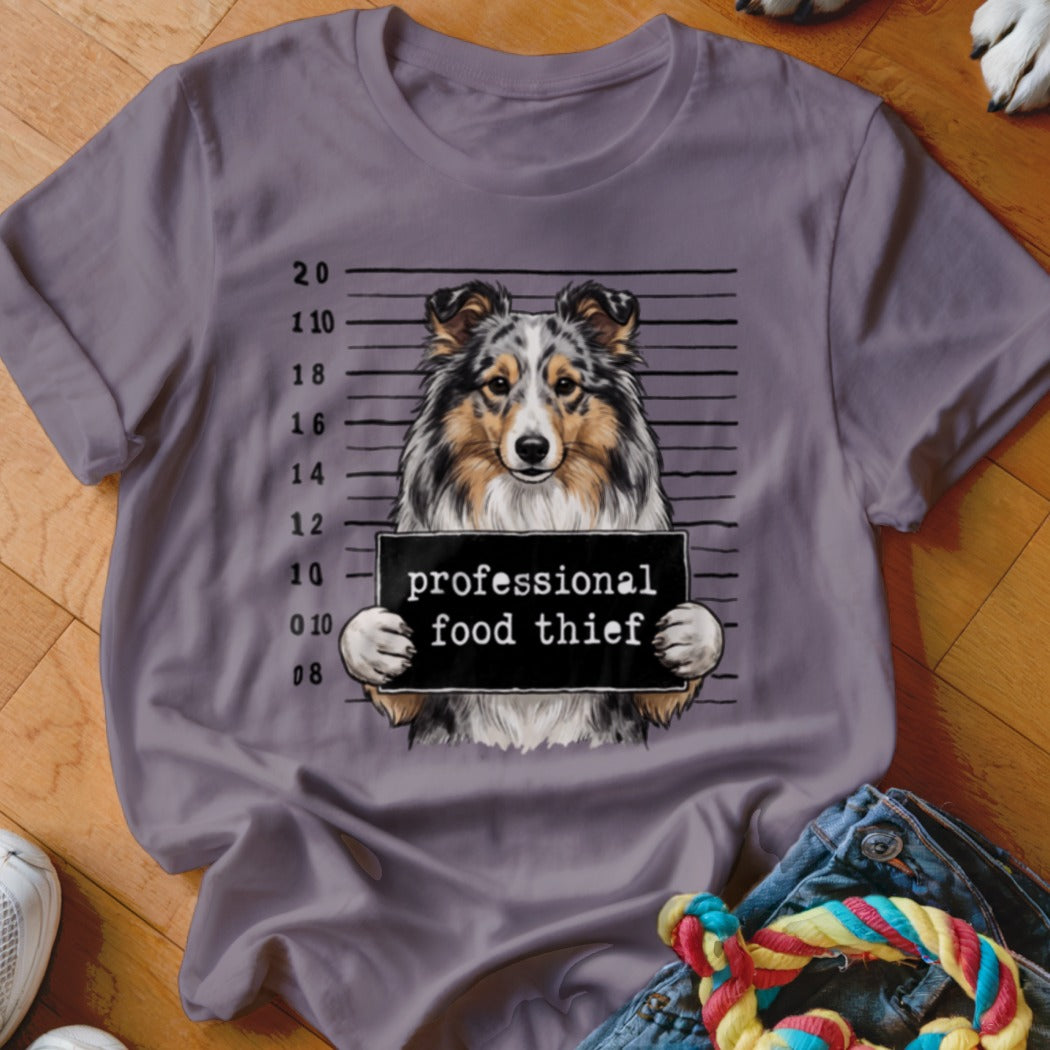 Sheltie dog mugshot with sign that says "professional food thief".