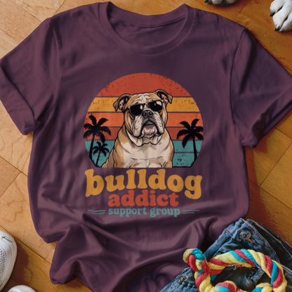 Maroon t-shirt featuring a retro sunset graphic of a bulldog wearing sunglasses with palm trees and text reading bulldog addict support group.