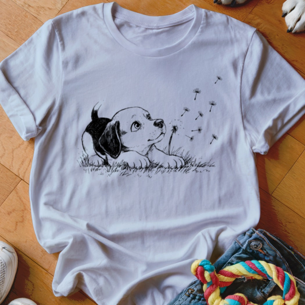 A white t-shirt featuring a black and white sketch of a puppy watching floating dandelion seeds.