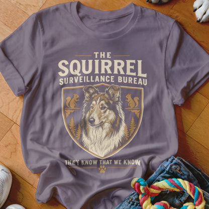 A purple t-shirt featuring a crest with a dog, squirrels, trees, and text that reads The Squirrel Surveillance Bureau.