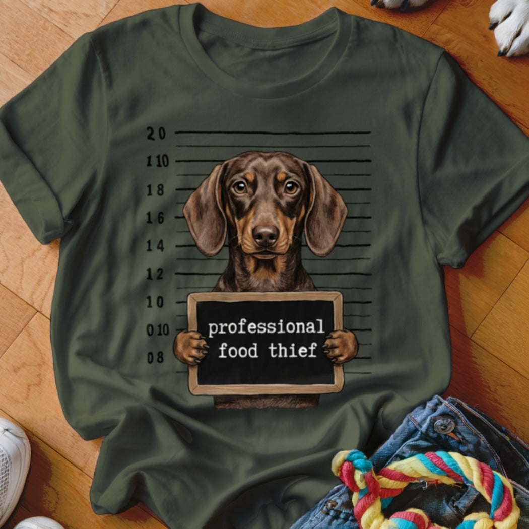 Dachshund mugshot with sign reading "professional food thief" on a green t-shirt.