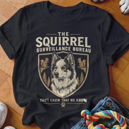 A black t-shirt printed with a crest featuring a dog, squirrels, and the text The Squirrel Surveillance Bureau.