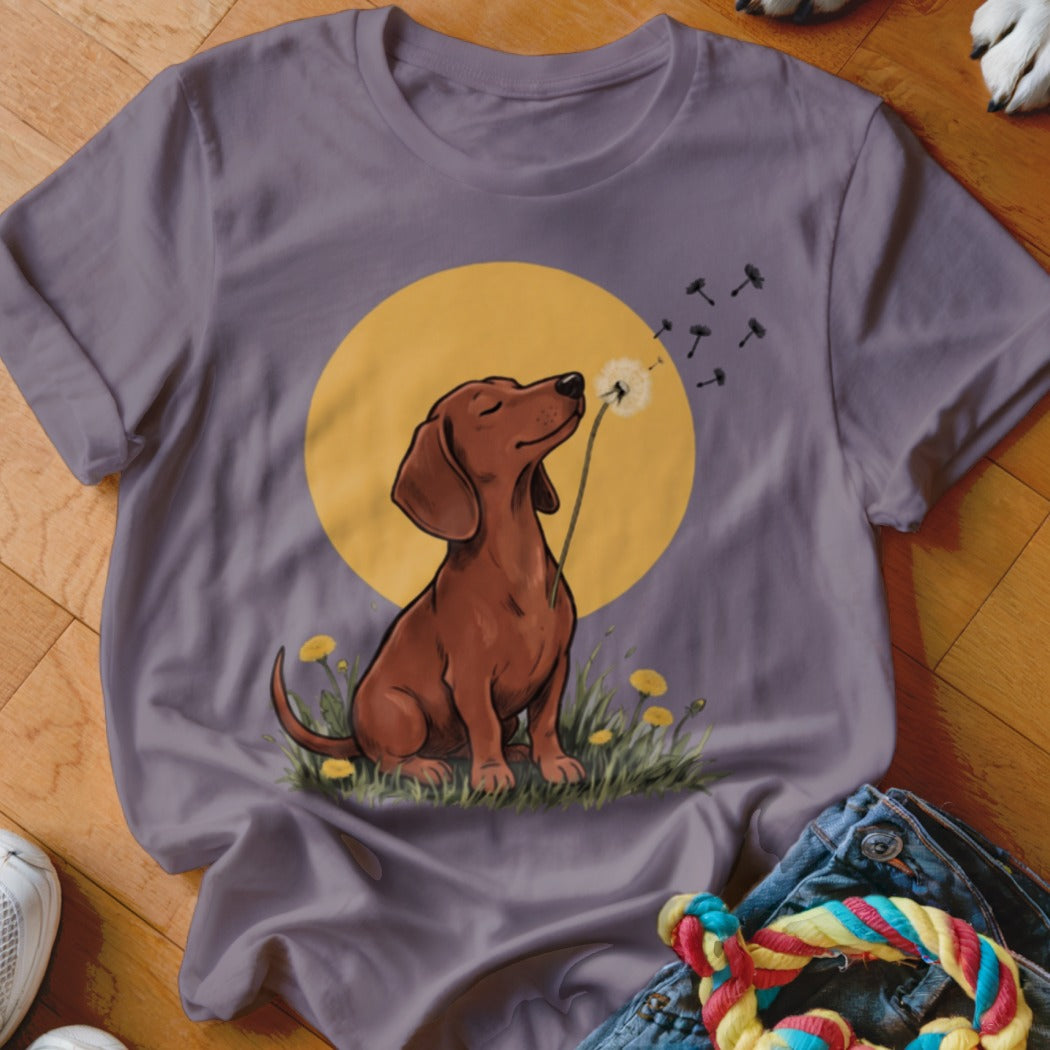 Gray t-shirt featuring an illustration of a brown dachshund blowing a dandelion against a yellow sun.