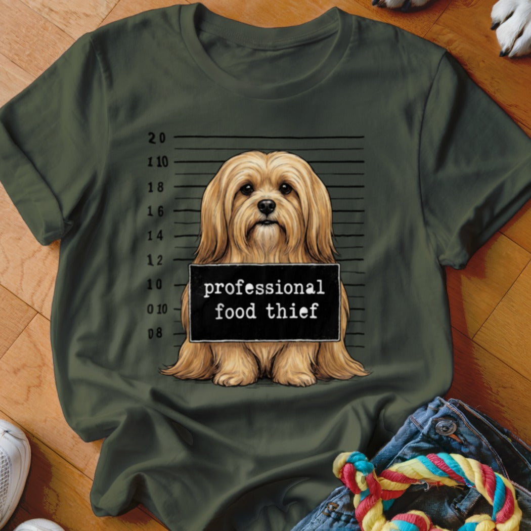 Dog mugshot with "professional food thief" sign on green t-shirt.