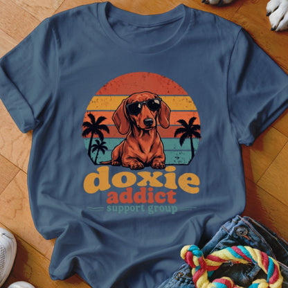 Dark blue t-shirt featuring a dachshund in sunglasses over a sunset and palm tree graphic with text.
