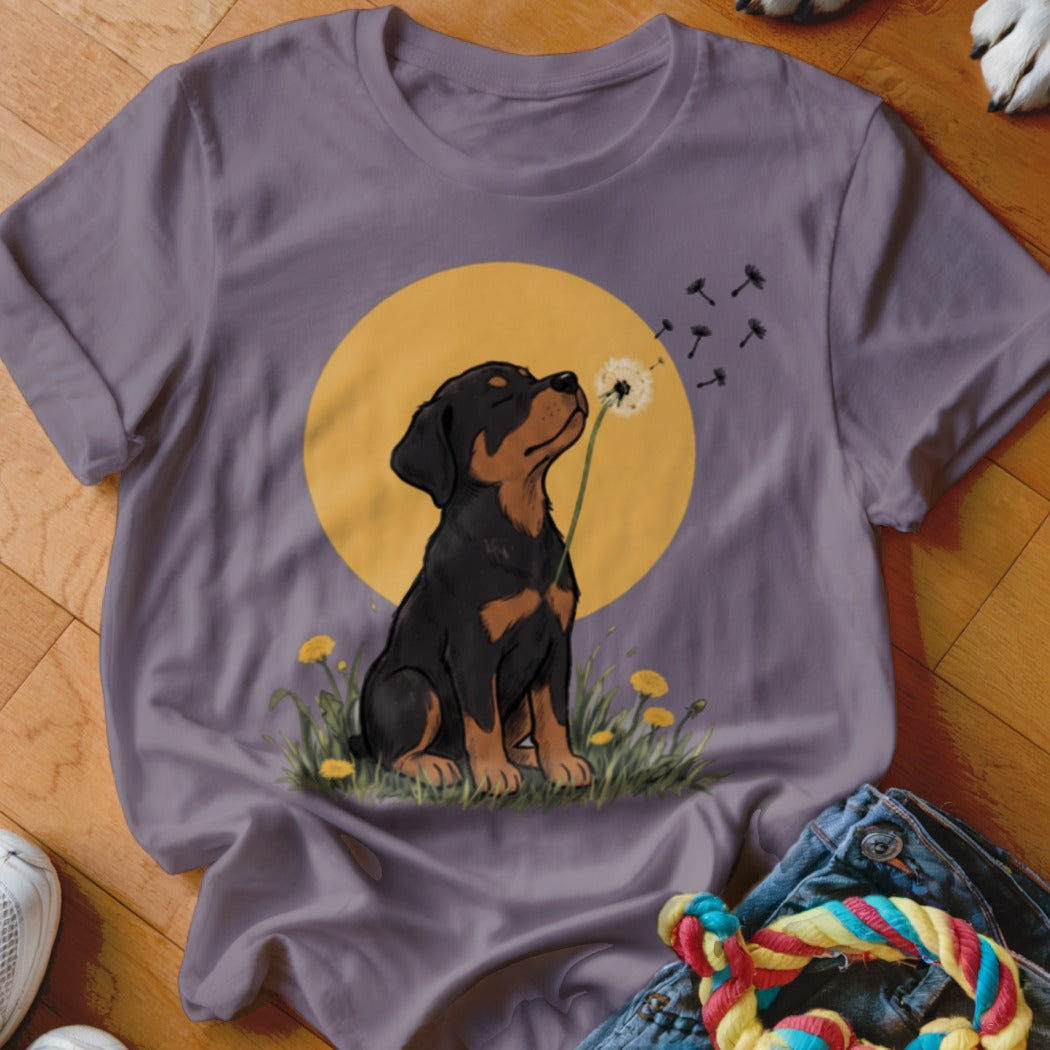 A mauve t-shirt with a graphic of a Rottweiler puppy sniffing a dandelion against a yellow sun.