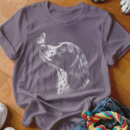 A purple crewneck t-shirt featuring a white line drawing of a spaniel looking at a butterfly on its nose.