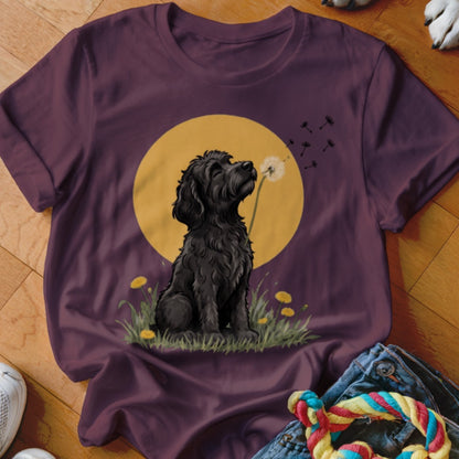 Maroon t-shirt featuring an illustration of a black dog sitting in the grass sniffing a dandelion.