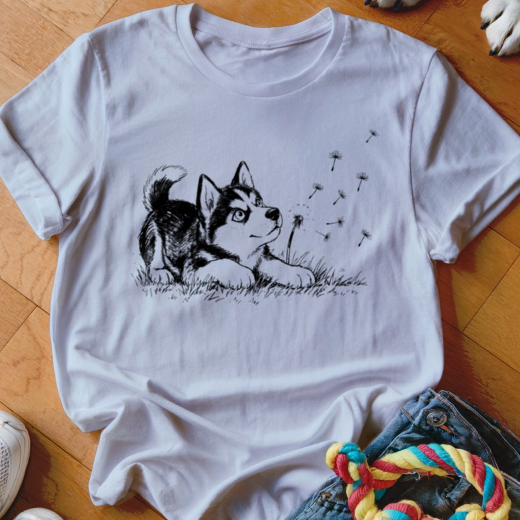 A white crewneck t-shirt featuring a black line drawing of a puppy watching floating dandelion seeds.