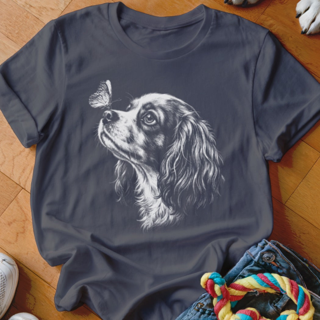 A dark grey t-shirt featuring a white line drawing of a spaniel looking at a butterfly on its nose.