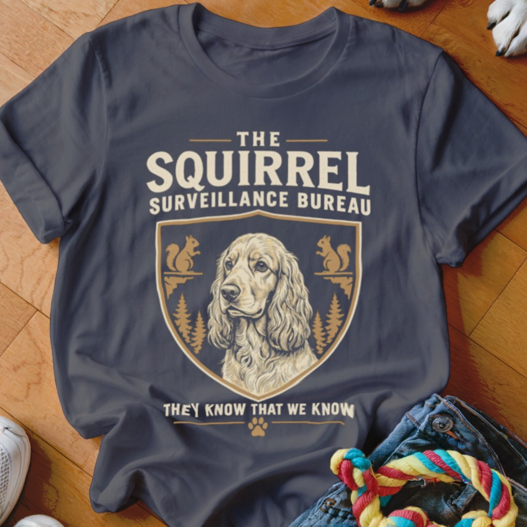 A dark grey t-shirt featuring a crest with a dog illustration and the text The Squirrel Surveillance Bureau They Know That We Know.
