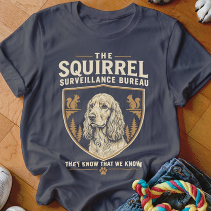 A dark grey t-shirt featuring a crest with a dog illustration and the text The Squirrel Surveillance Bureau They Know That We Know.