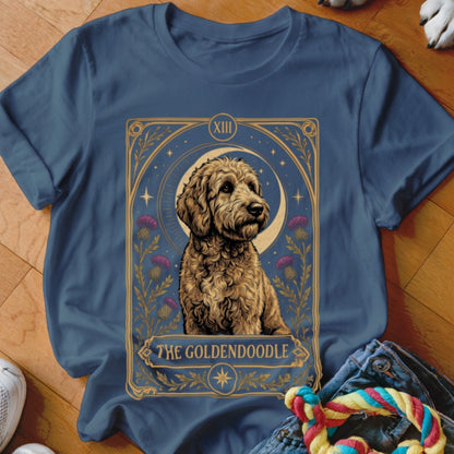 A blue t-shirt printed with a tarot card graphic featuring a goldendoodle, a crescent moon, and the text The Goldendoodle.