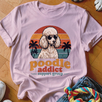 A light pink t-shirt featuring a retro graphic of a poodle wearing sunglasses in front of palm trees.