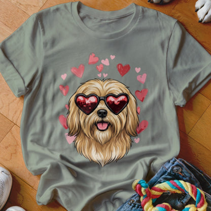 A sage green t-shirt featuring an illustration of a fluffy dog wearing heart-shaped sunglasses surrounded by pink hearts.