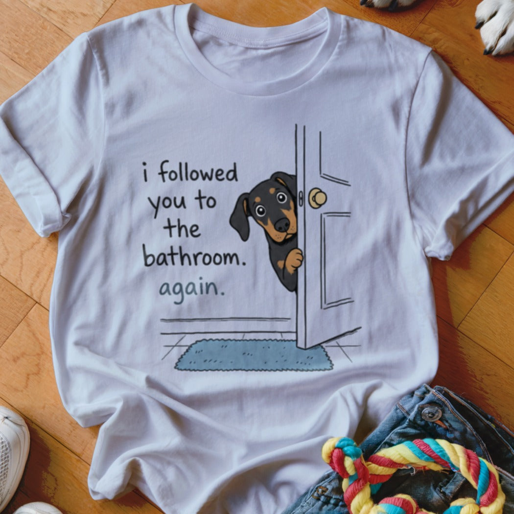 White t-shirt with a dachshund peeking through a door, text reads "I followed you to the bathroom. Again."
