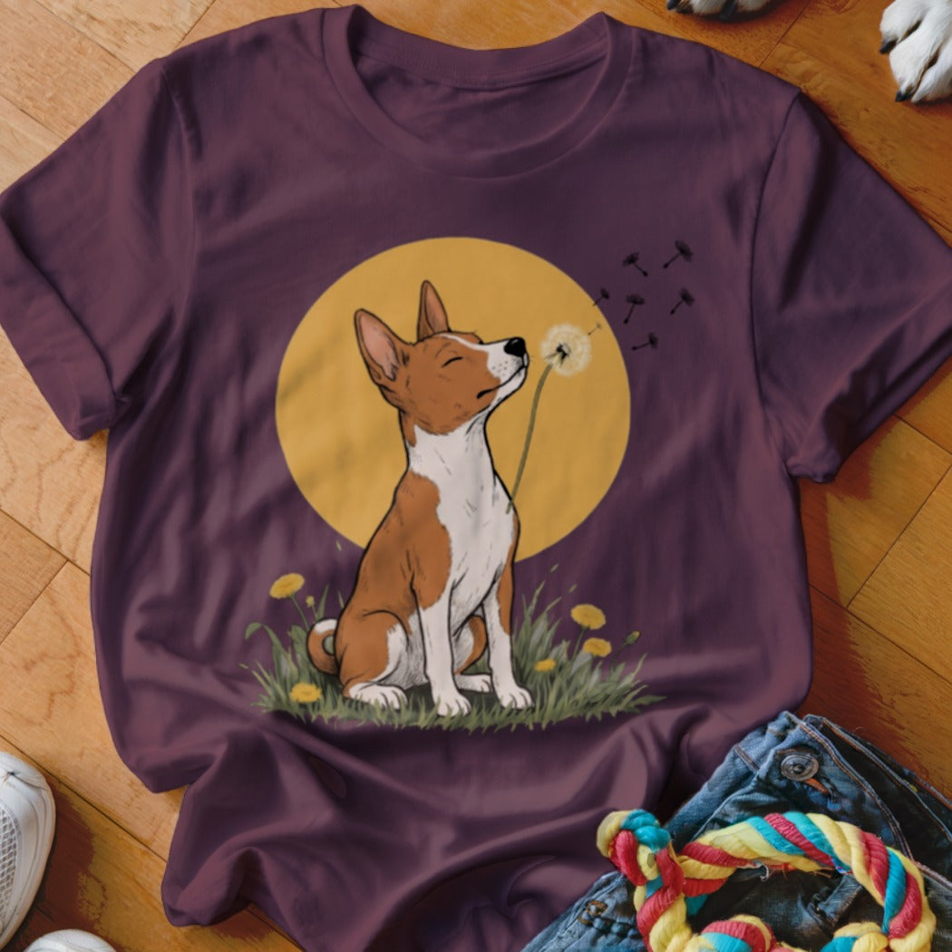 A dark purple short-sleeved t-shirt featuring a cartoon illustration of a Basenji dog blowing dandelion seeds in front of a yellow circle.