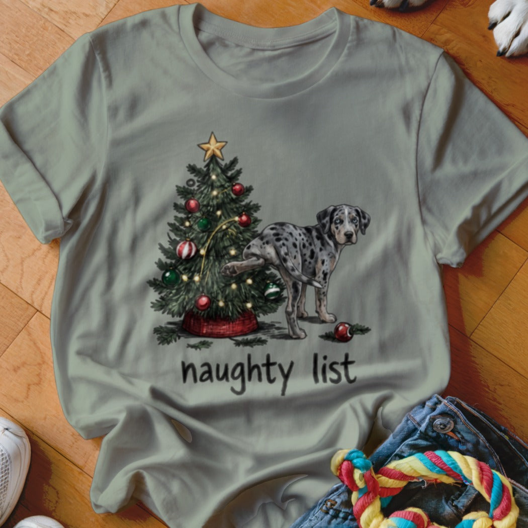 Sage green crewneck t-shirt featuring a spotted dog peeing on a Christmas tree with the text "naughty list".