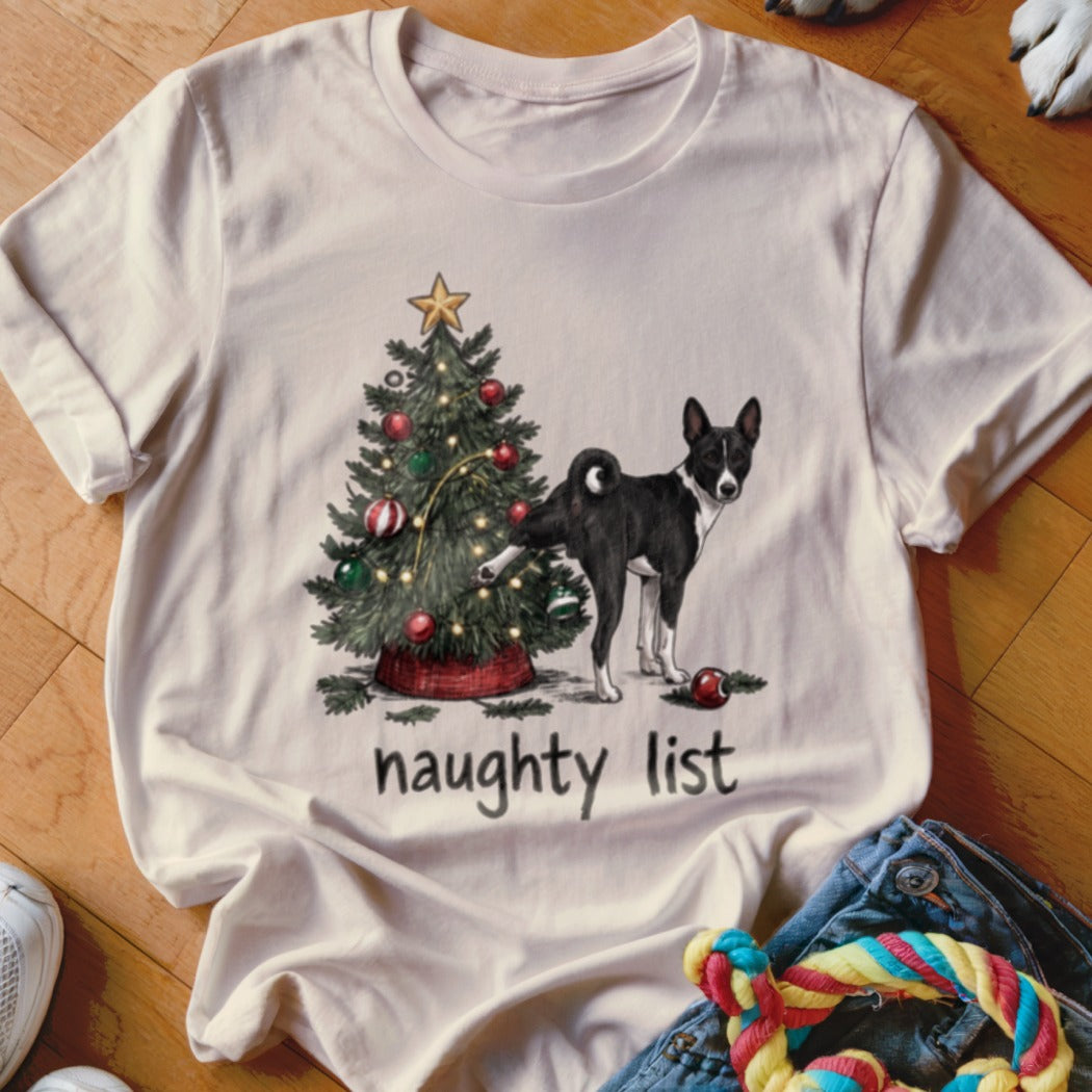 A light-colored t-shirt with a graphic of a black and white dog lifting its leg at a decorated Christmas tree, with the text naughty list underneath.