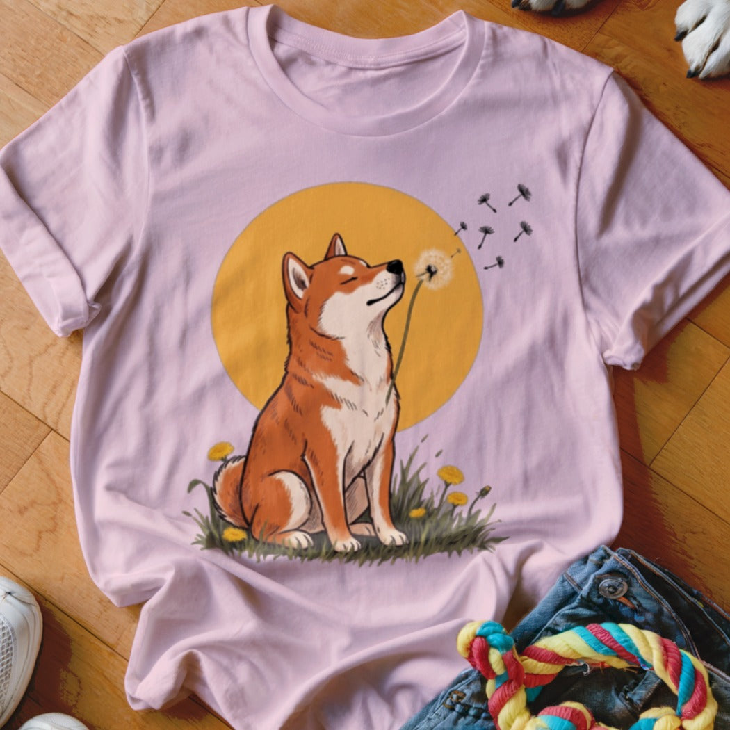Light pink t-shirt featuring a graphic of a Shiba Inu dog blowing dandelion seeds.